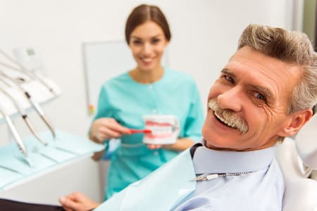 Man in dentist’s chair smiling with dentist in background
