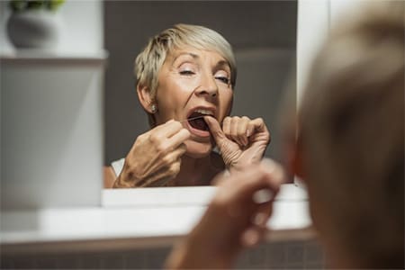 Woman flossing her teeth in the bathroom mirror