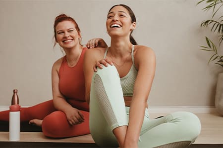 Two friends smiling while sitting in workout studio