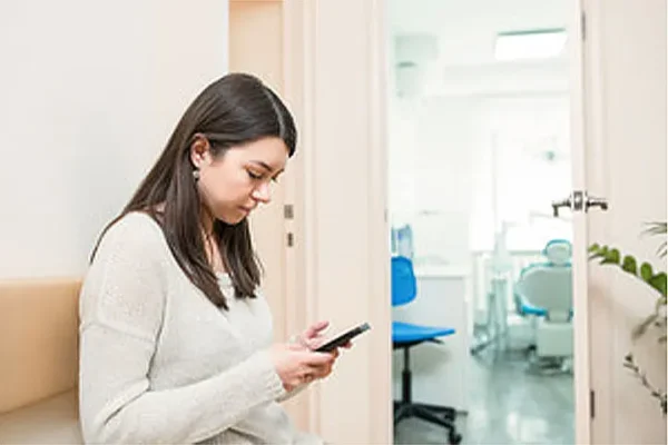 Woman in white shirt smiling and sitting in dental office waiting room
