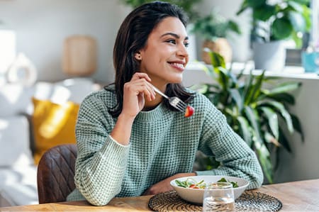 Woman smiling while eating healthy meal at home.